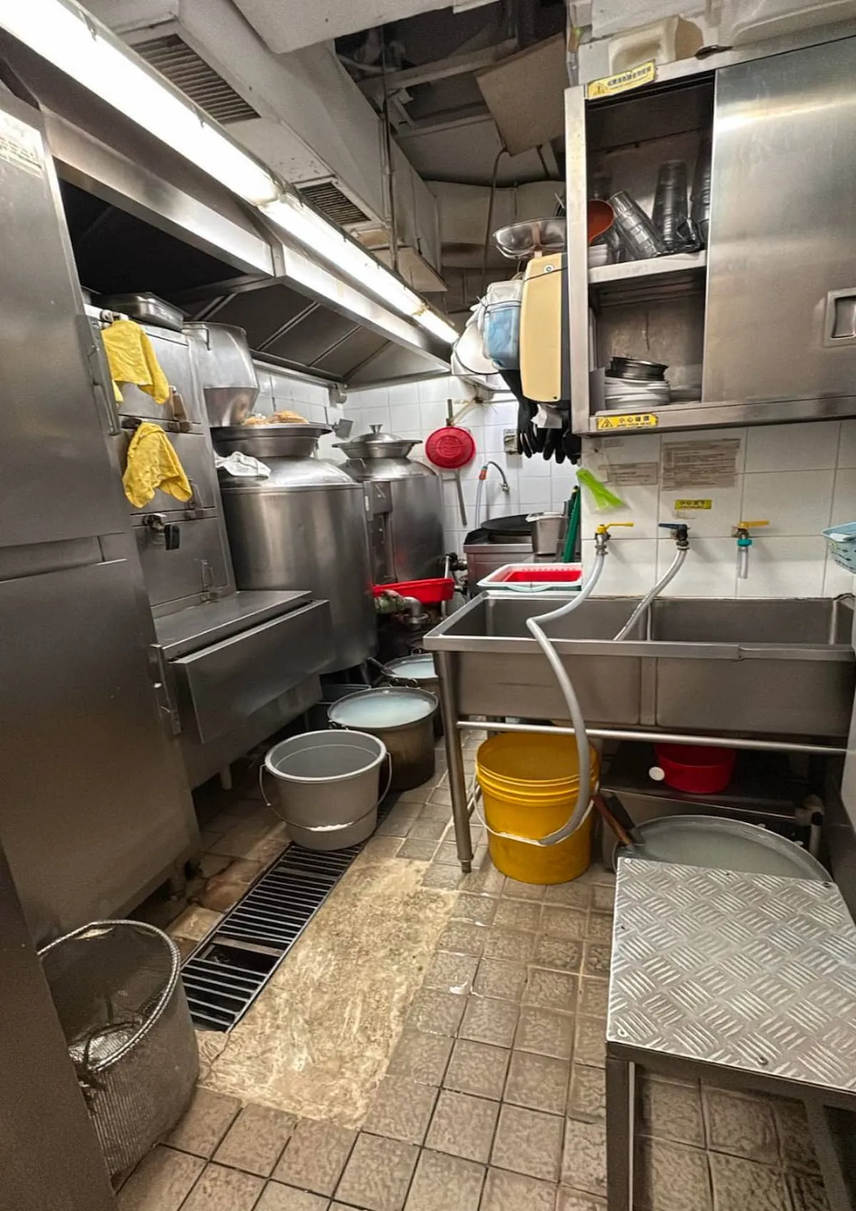 Ref#3625 is a commercial kitchen dishwashing area for restaurant rental, featuring stainless steel sinks, metal containers, cleaning supplies, yellow buckets, utensils, and a tiled floor with equipment and tools.