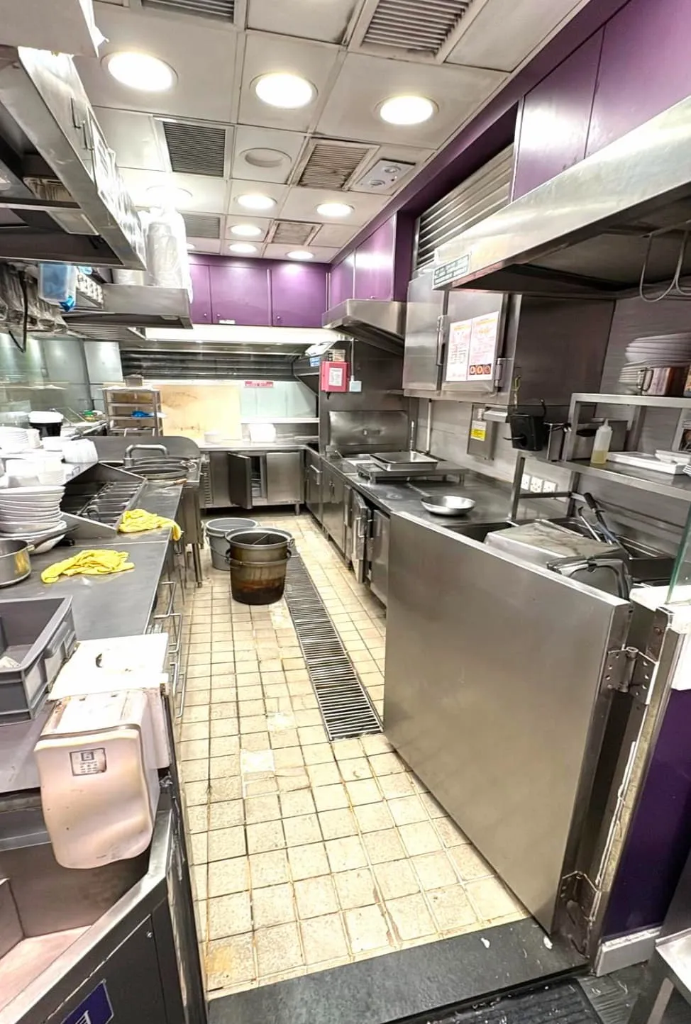 Ref#3625 is a commercial kitchen with stainless steel appliances, purple walls, metal shelves, and cooking equipment. It has a tiled floor with a central bucket and counters stocked with utensils and supplies
perfect for restaurant rental.