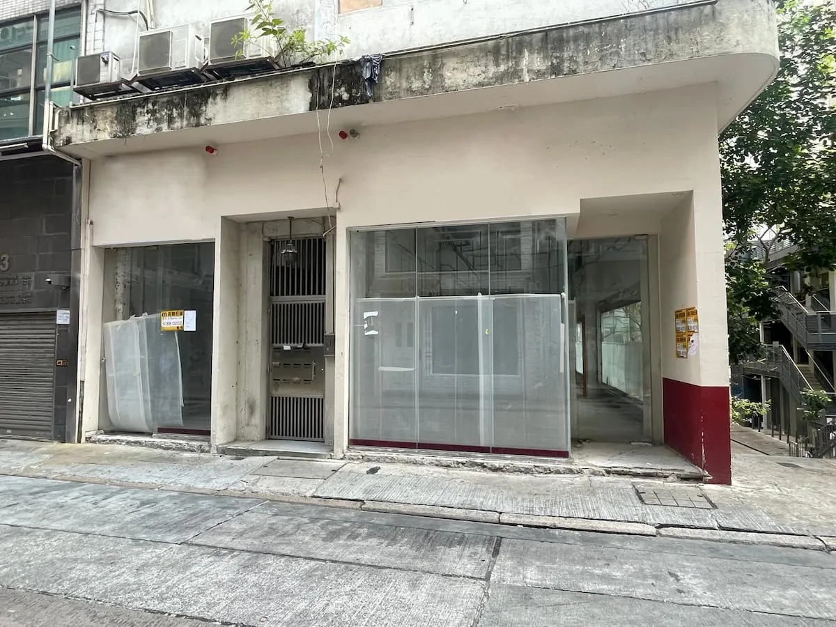 Ref#3626 is a weathered building on a sloped street, featuring large windows with semi-transparent plastic sheets, a central metal door, and "rent shop" signsideal vacant storefront for your next venture.