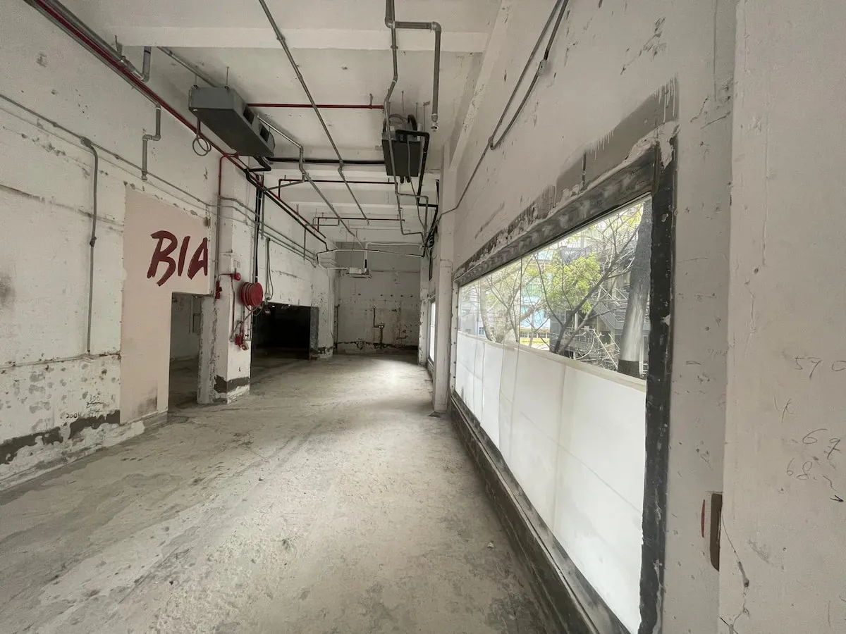 Ref#3626 is an empty, unfinished space perfect for office or shop rental, with exposed pipes, rough concrete floors, and large windows. "BIA" is boldly painted in red on the sunlit left wall.