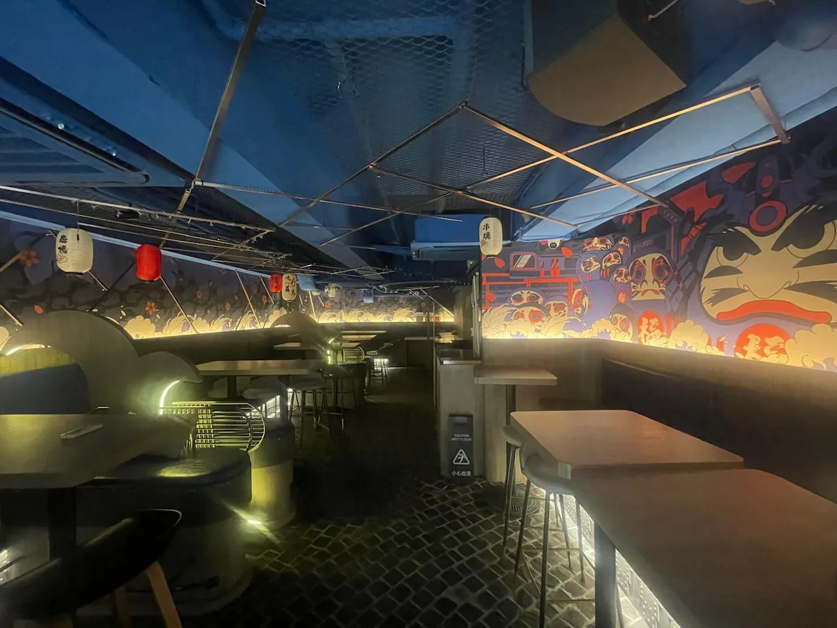 Ref#3627 offers a modern restaurant interior for rent, featuring dim lighting, blue walls with vibrant Japanese-style murals, cozy booth and table seating, hanging lanterns, and under-table lightingideal for your next shop or restaurant venture.