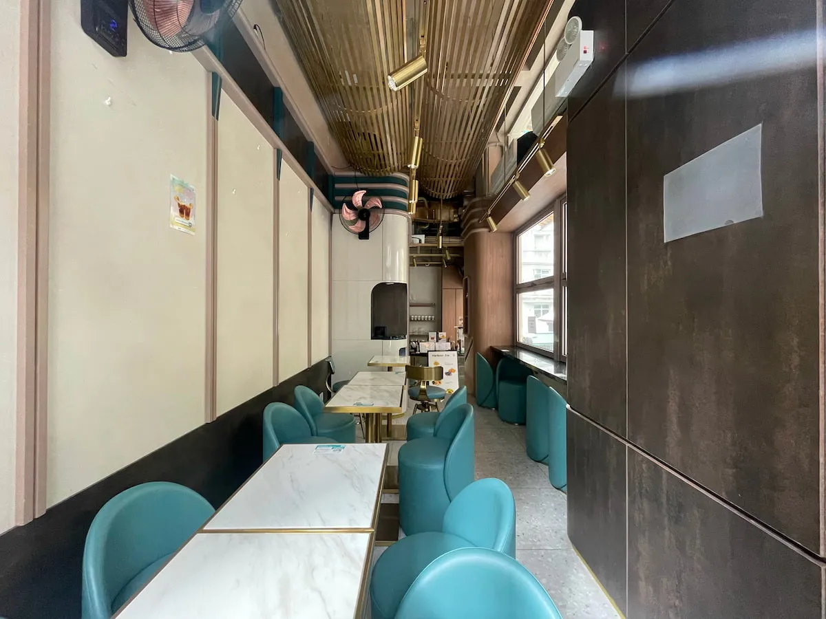 Ref#3634 showcases a modern cafe9 interior ideal for restaurant rental, featuring teal chairs, white marble tables, window counter seating, exposed piping, and gold ceiling accents in an open, empty space.