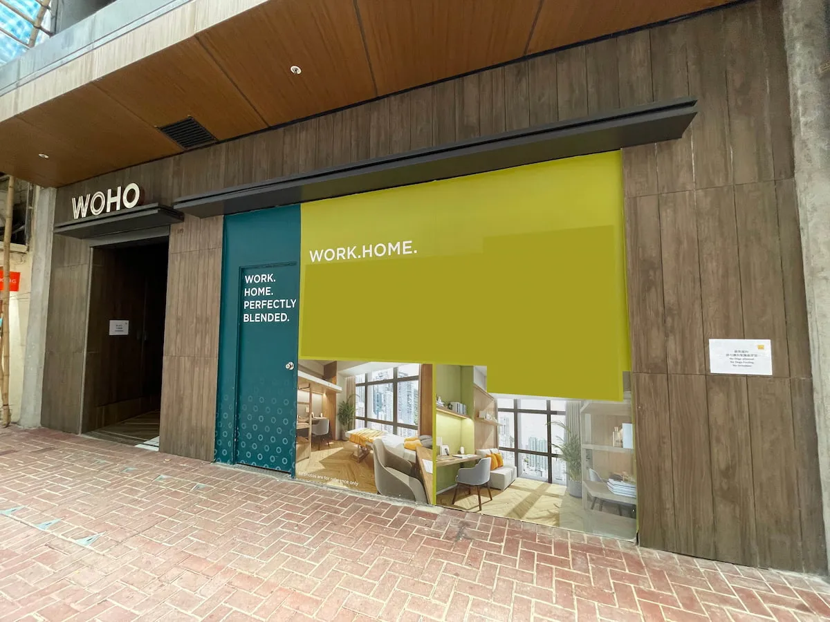 Storefront with WOHO sign and green-yellow panel "WORK.HOME. PERFECTLY BLENDED,” showing a modern living workspace (Ref#3635)—ideal to rent for office or shop space on a brick walkway.