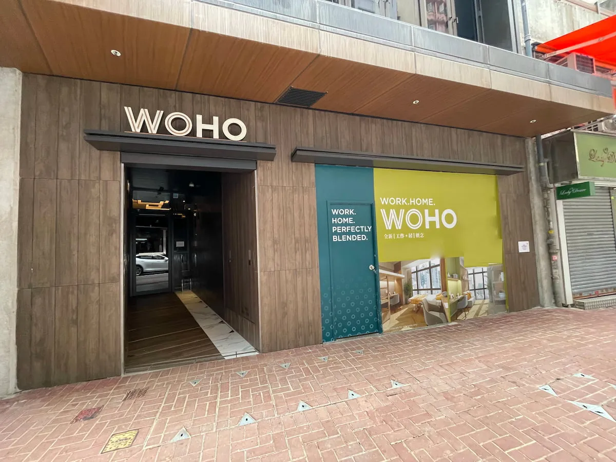 A building entrance with a sign reading WOHO. Beside it, a large window displays: WORK. HOME. WOHO.—blending both for flexible shop or office rental, as seen in Ref#3635’s inviting co-working and living interiors.
