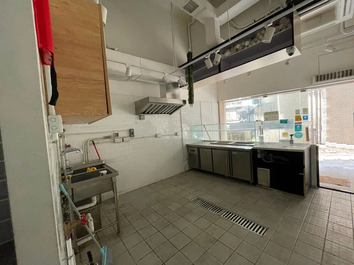 Ref#3638: Vacant commercial kitchen with tiled floors, stainless steel sink, counters, ventilation hood, large windows for natural light, empty prep area, and display counter0ideal to rent as a restaurant.