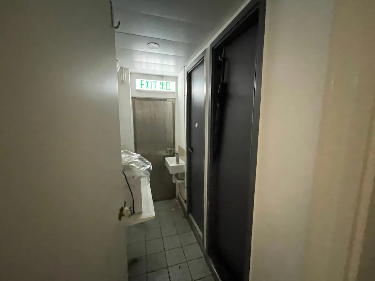 Ref#3638: Narrow hallway with tiled floor, small sink, mirror, and dark doors0perfect for office rental. A green EXIT sign is above the metal door at the end.