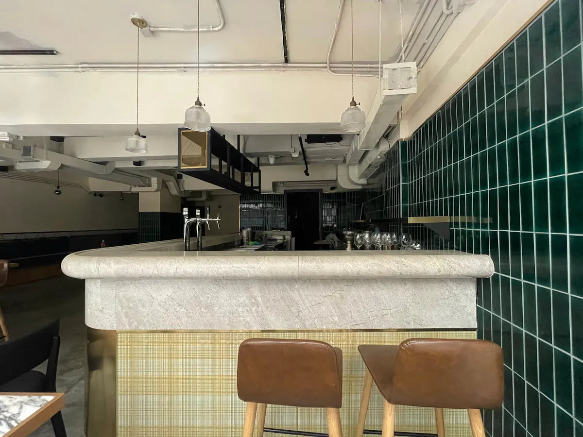 Ref#3640 is a modern, empty bar featuring a marble countertop, brown stools, green tiled walls, and pendant lightsperfect for restaurant rental. This clean, minimalistic space offers a stylish setting with no people present.