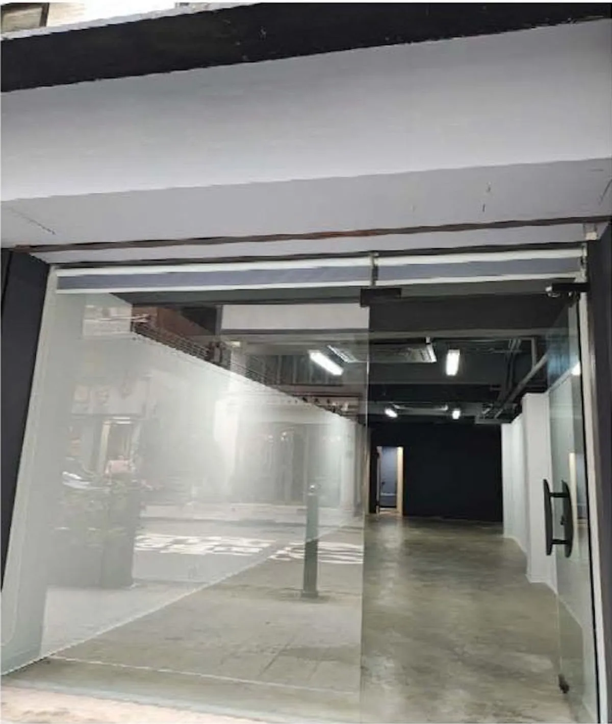 Ref#3645 features a glass storefront with a sliding door, concrete floors, modern white and dark walls, and ceiling lights2creating an empty, stylish interior ideal for use as a shop, office, or restaurant.
