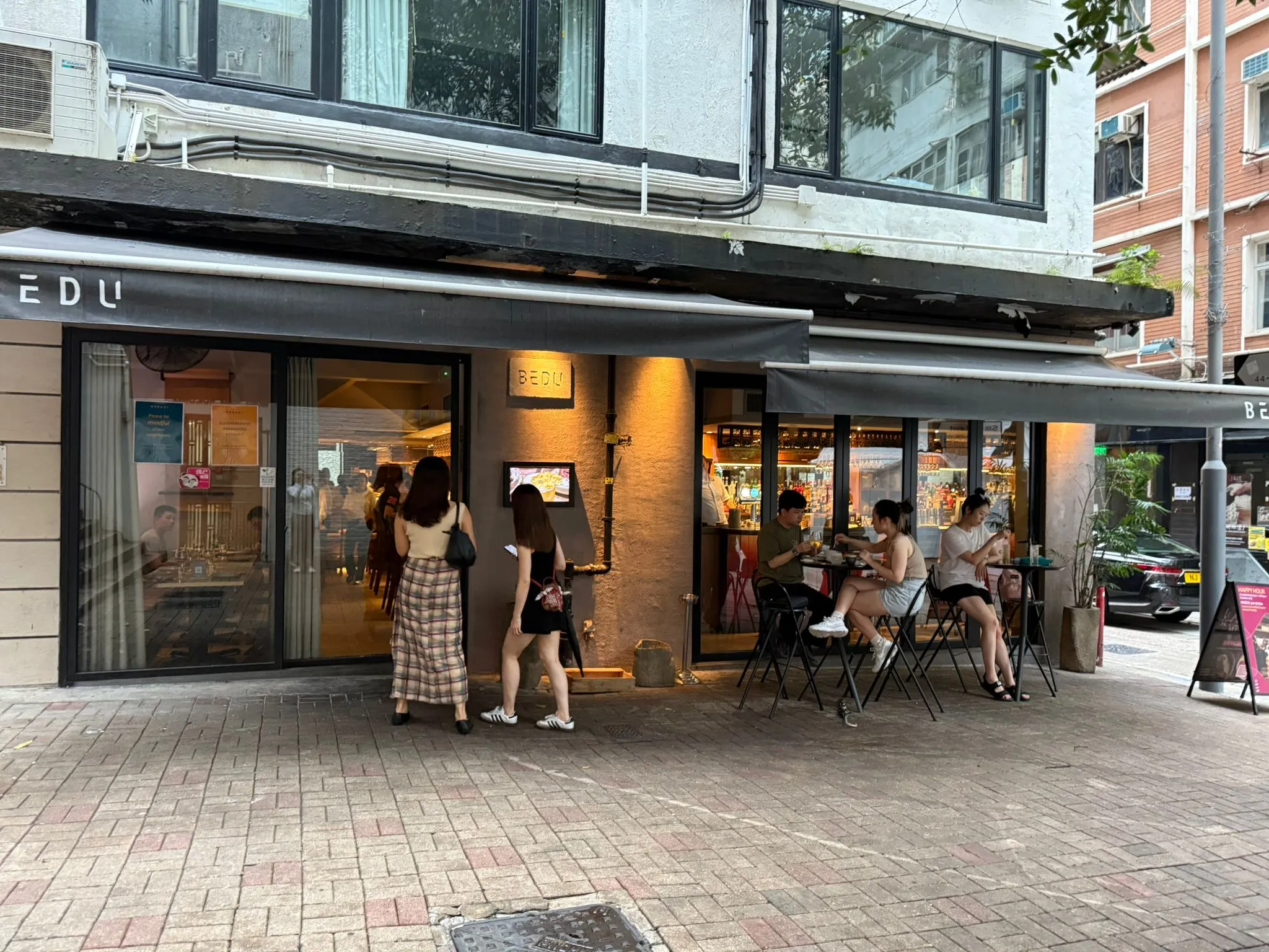 Ref#3654: Street-view cafe with large windows and outdoor seating, perfect for restaurant space rental. People enjoy food and drinks at tables, creating a lively and casual atmosphere.