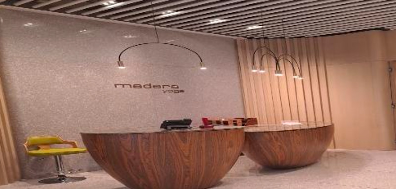 Ref#3663 features a modern yoga studio reception with two large round wooden desks, a green chair, pendant lights, and a "madera yoga" wall sign. Vertical wood paneling and neutral tones complete this perfect office or shop rental.