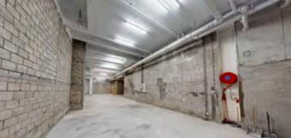 Ref#3662: A spacious concrete hallway with brick and cement walls, overhead fluorescent lights, exposed pipes, and a red fire hose
perfect for industrial-style office or unique shop rental.