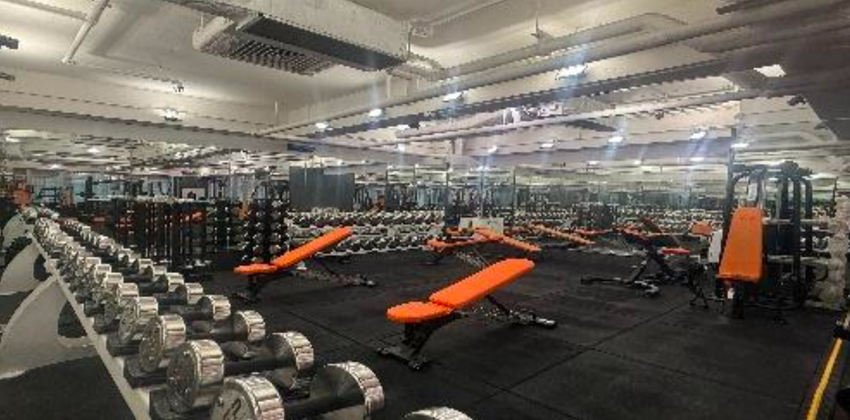 Ref#3660: A spacious gym with silver dumbbells, orange benches, weight machines, and mirrored walls—brightly lit and ideal for renting shop or office space in a fitness-focused setting.