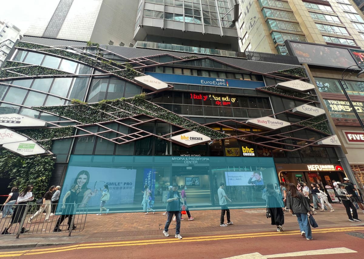 Ref#3658: Modern commercial building with glass façade, green vines, multiple signboards, and a prominent digital display above the entrance—ideal for renting office or shop space in a bustling street location.