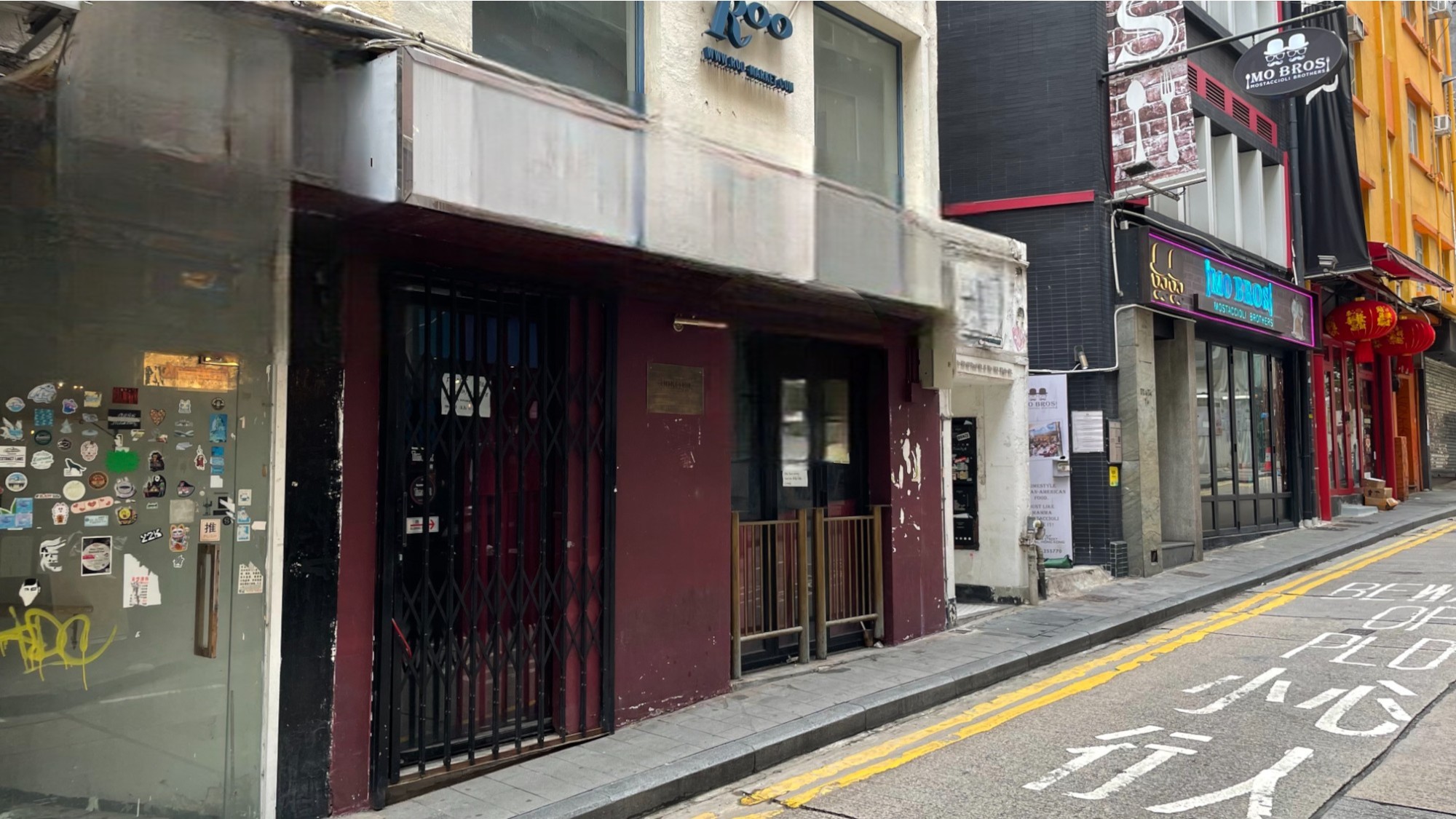 Ref#3643 is located on a narrow city street with closed shops, a sticker-covered electrical box, and English and Chinese signs. The empty, yellow-lined street features restaurants and businesses252;perfect to rent as a shop or restaurant.