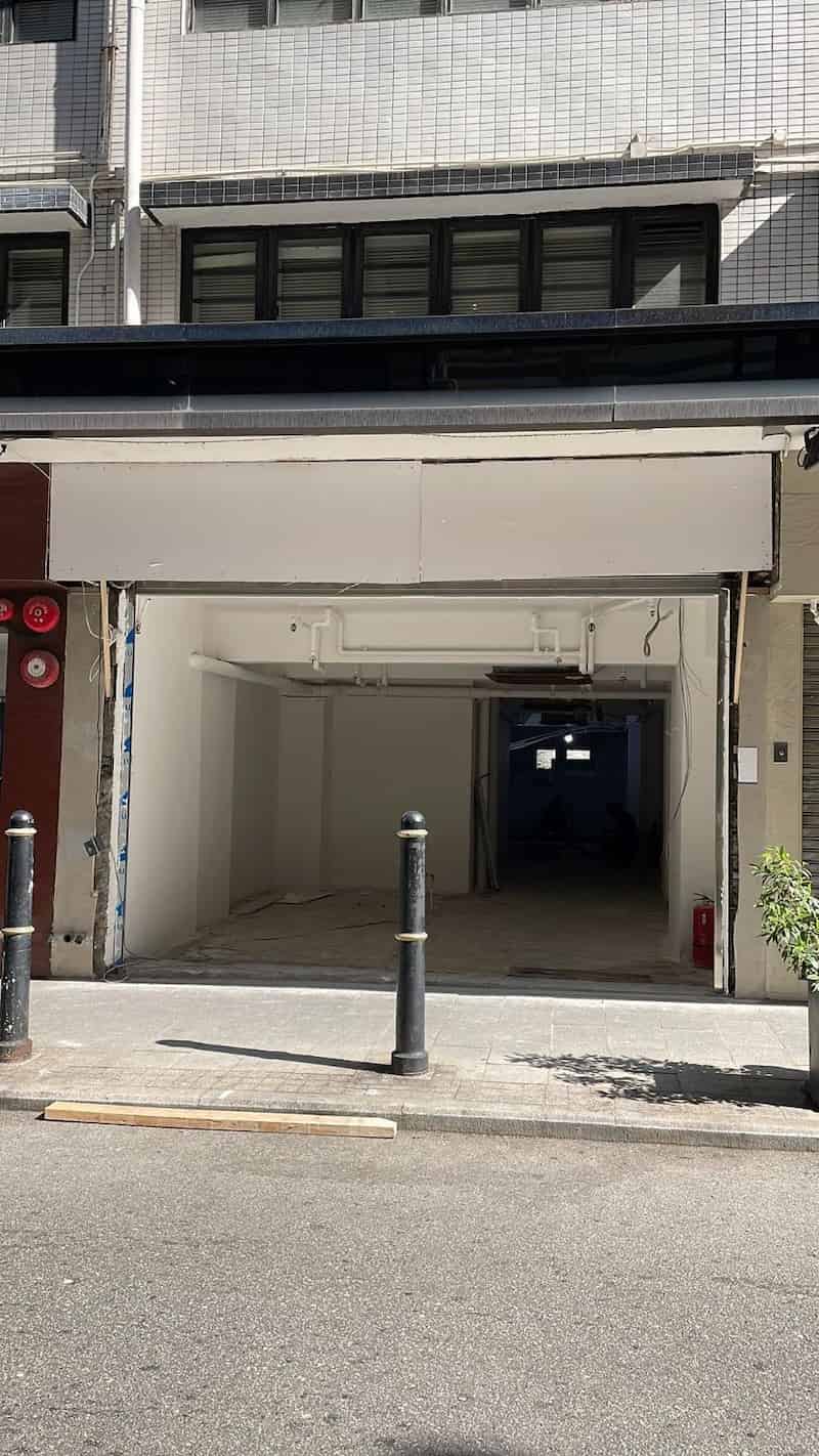 Ref#3646: Vacant open garage space with white walls and ceiling, perfect for use as an office, shop, or restaurant. Two black bollards mark the entrance; sunlight creates shadows on the concrete floor.