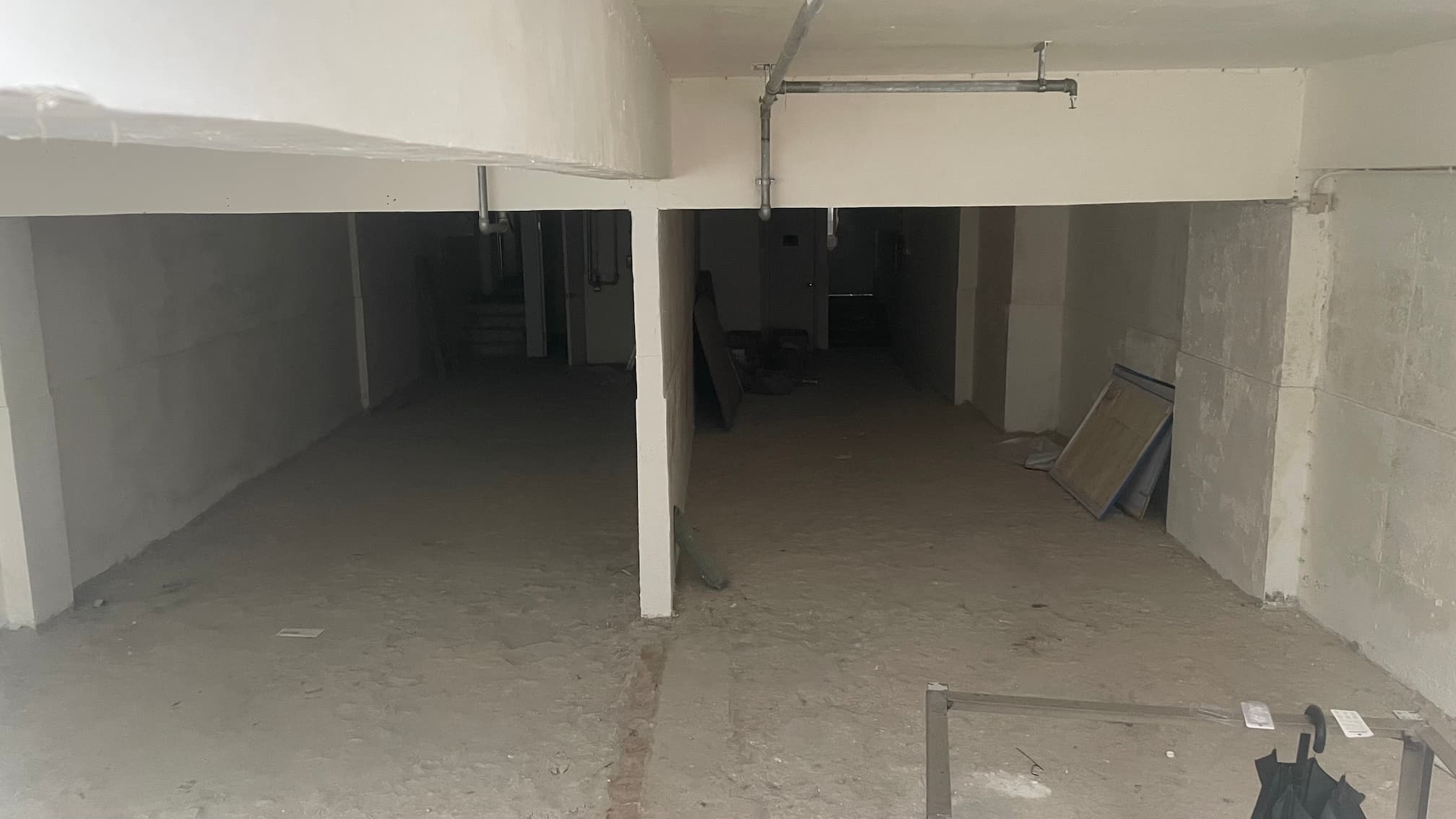 Ref#3644 features a dim, unfinished basement or parking area with concrete floors, white walls, two large openings separated by a column—perfect for office or shop rental. Construction materials are scattered on the right side.