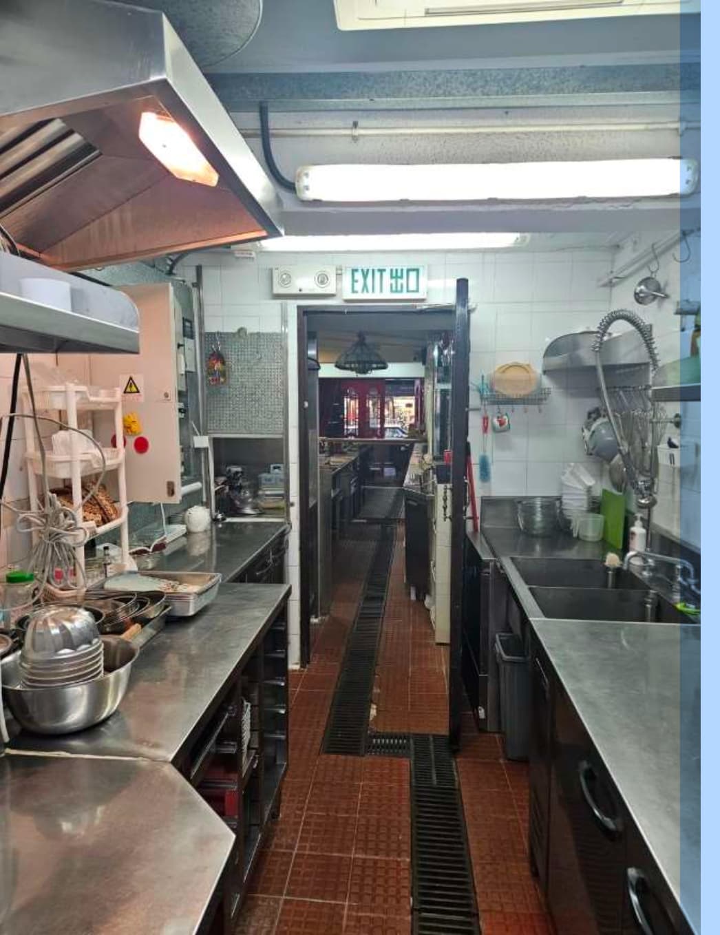 Ref#3632 is a clean, organized commercial kitchen for rent featuring stainless steel counters, diverse cooking equipment, tiled floors, and an illuminated EXIT sign above the back door for safety and efficiency.