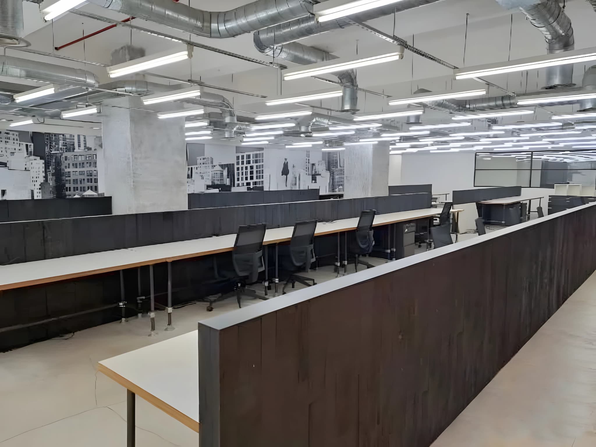 Ref#3617: A modern, open-plan office for rent with rows of desks and black chairs, LED lighting, exposed ducts, and black-and-white cityscape wall art in the background.
