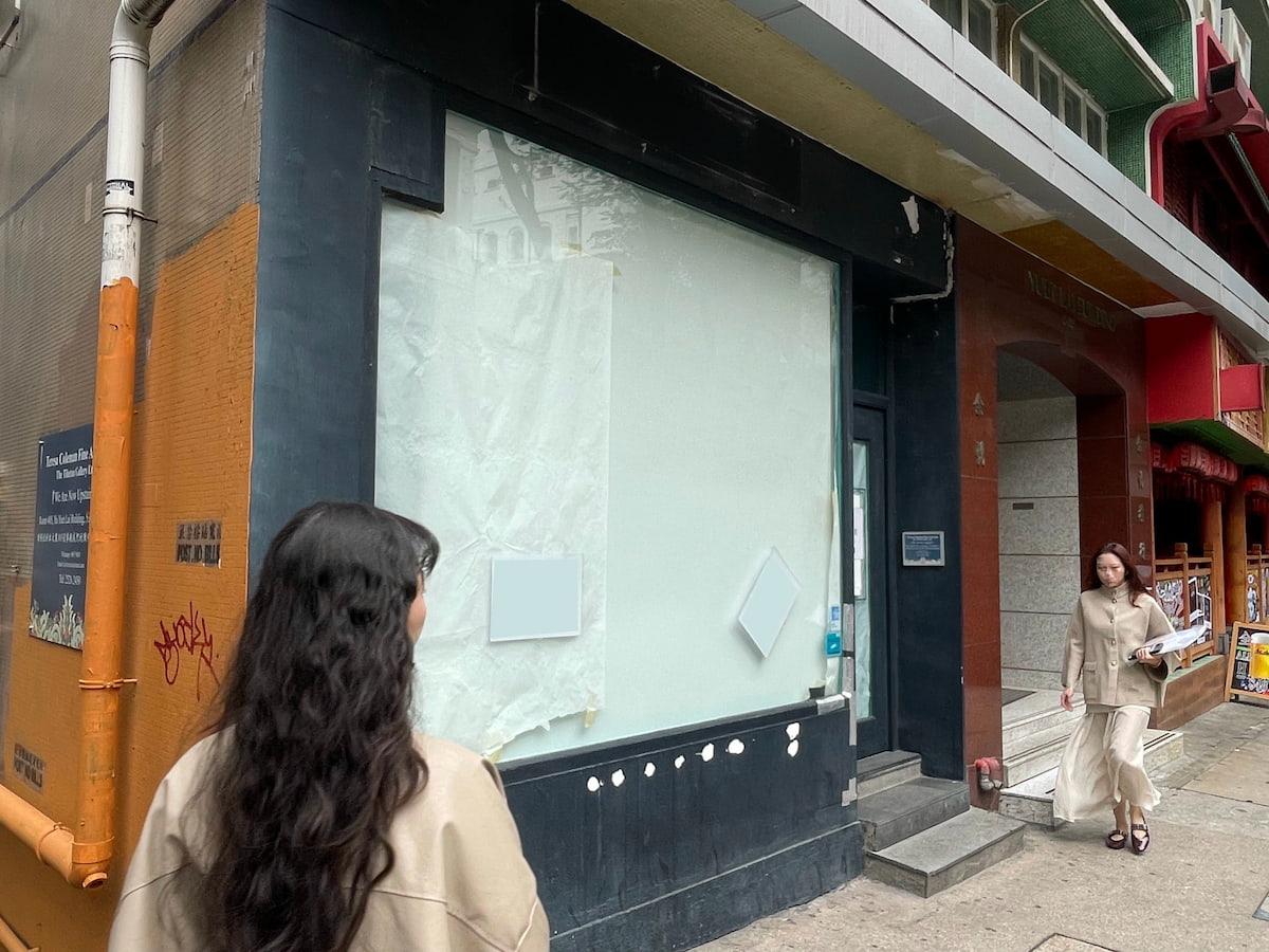 Two women in beige outfits walk past the vacant Ref#3619 storefront with covered windows. One holds papers and wears a face mask, suggesting the shop may be available for rental or renovation.