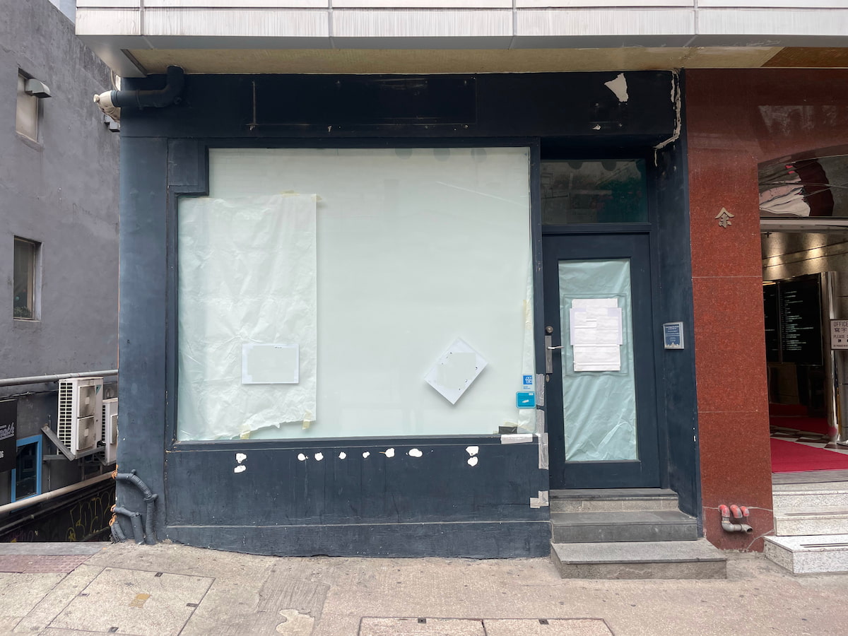 Ref#3619: Vacant storefront with covered windows and door, perfect to rent as an office or shop. Features a dark façade with some peeling paint, notices on the glass door and window, and steps from the sidewalk to the entrance.