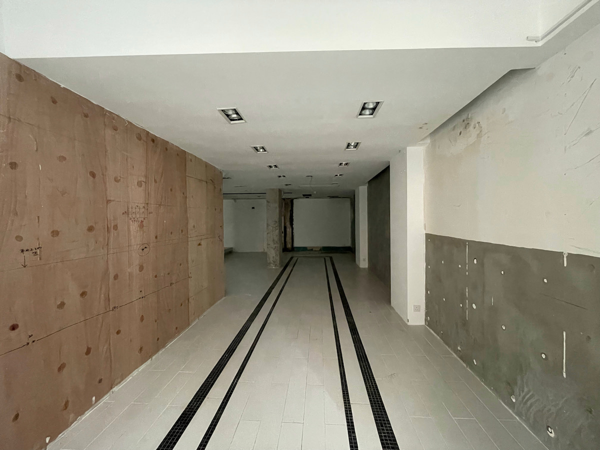 Ref#3618: Spacious, unfinished room with tiled floors, exposed concrete and drywall walls, and strip lighting15perfect to rent as a shop or office while under renovation or construction.