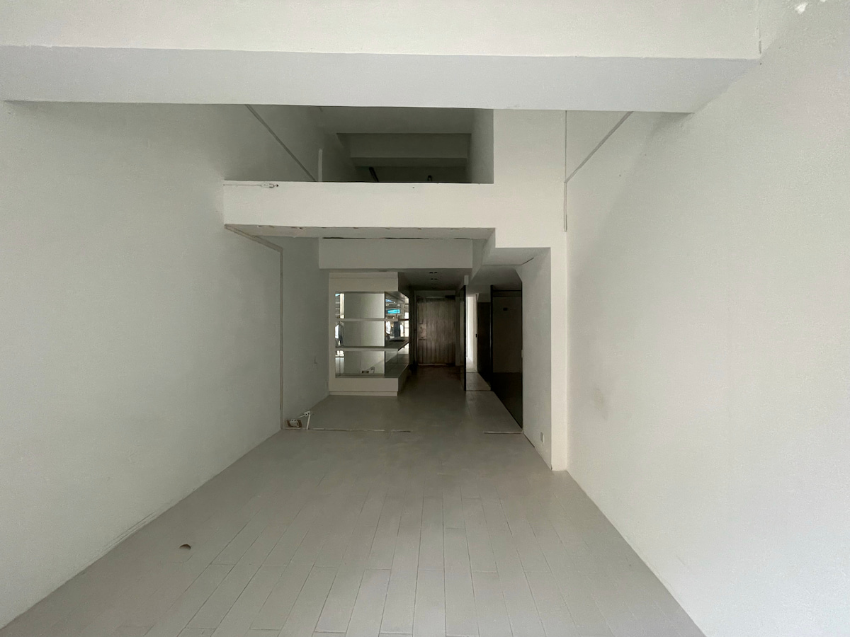 Ref#3618: Spacious, unfurnished white-walled room with light wood flooring, high ceiling, open mezzanine, and doorway to another area15ideal for a rental shop or office.