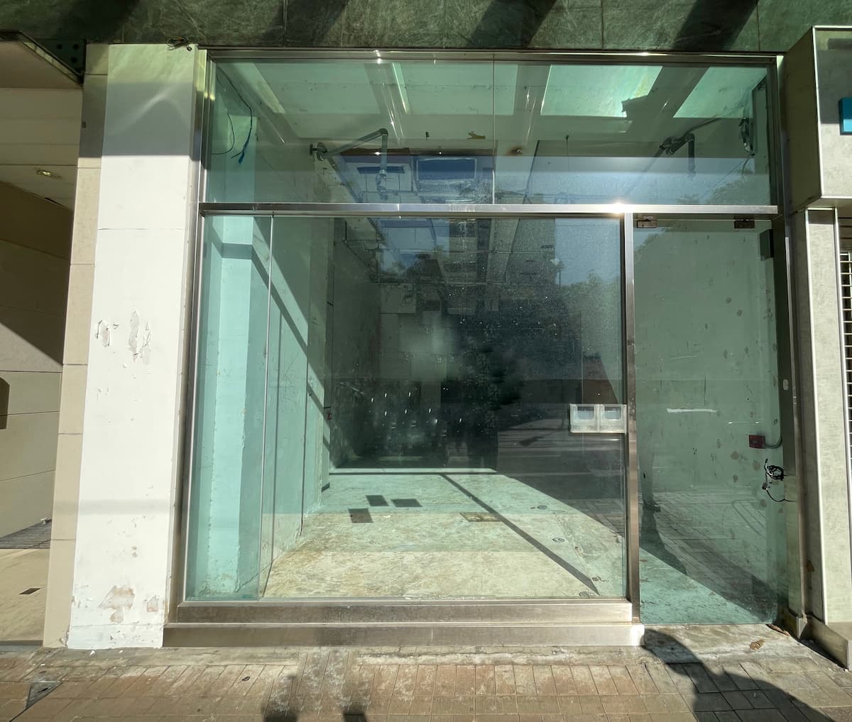 Ref#3604: Sunlit, empty storefront with large glass windows and door, ideal for shop rental. Features an unfinished interior with bare floors and walls, reflecting the street outside.