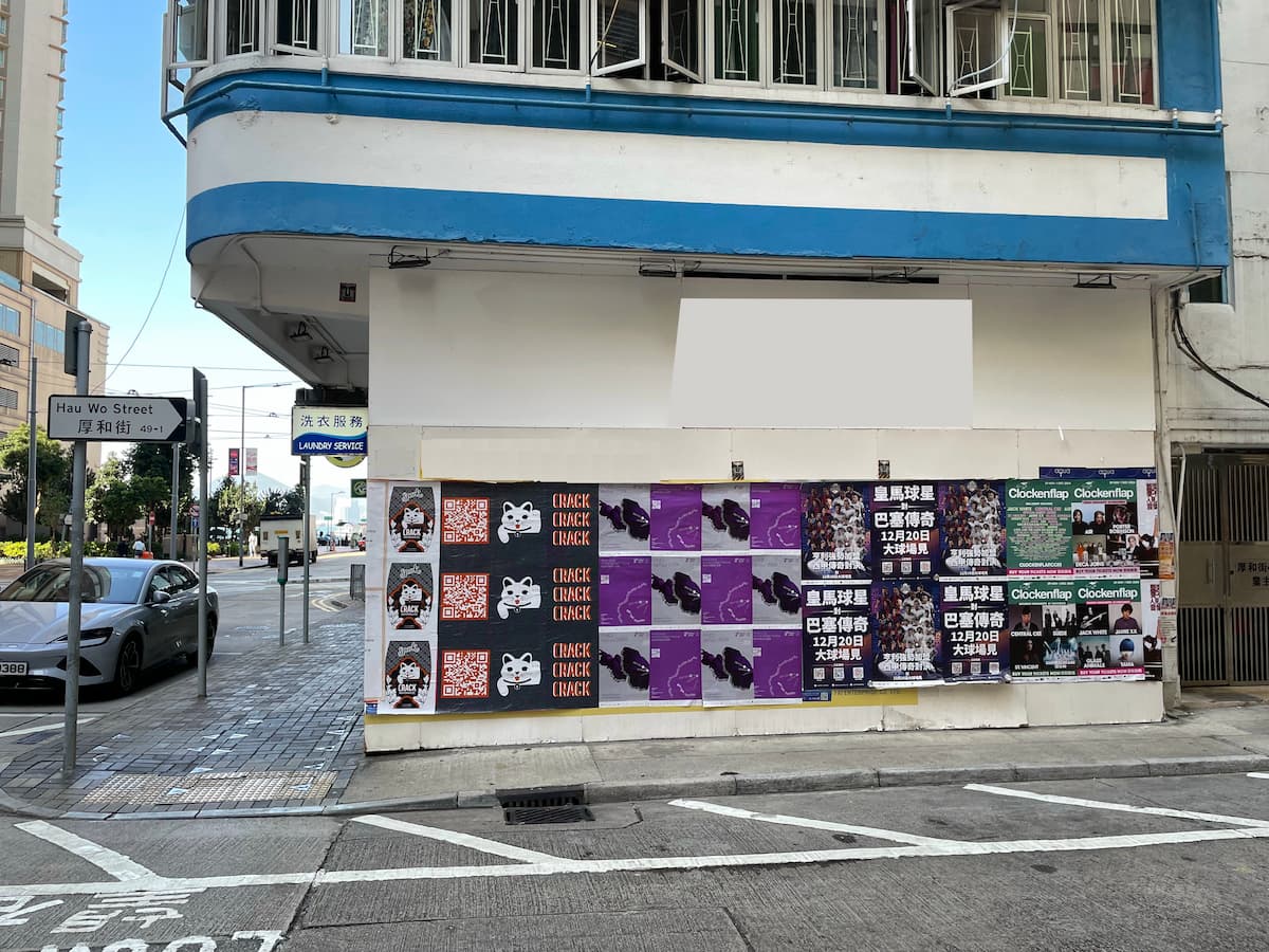Ref#3607 is a white building on a quiet corner of Hau Wo Street, featuring colorful posters and ads on its lower wall	64ideal for shop rental with minimal foot and car traffic in the area.