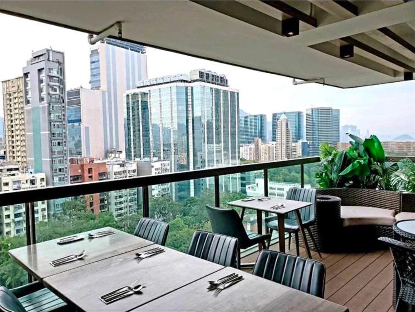 Ref#3612: A rooftop restaurant terrace with set tables and chairs overlooks a cityscape of modern skyscrapers, featuring lush greenery and plantsideal for those seeking unique restaurant rental options.