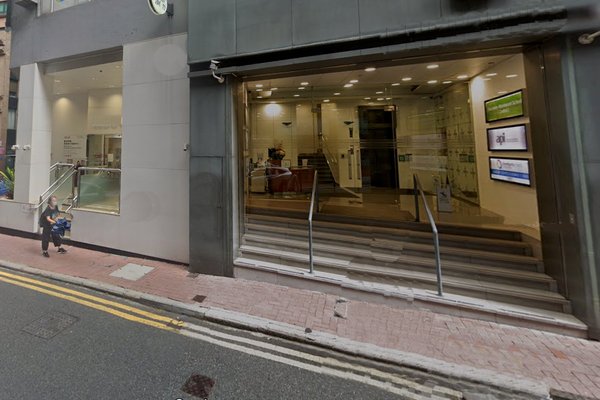 Ref#3210 features a modern entrance with wide glass doors, steps with handrails, a sloped sidewalk to the left, and a bright interiorideal for office rental. A person sits on the curb nearby.