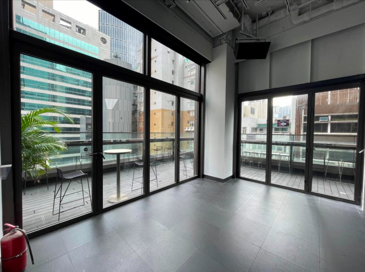 Ref#3601: Modern empty room with floor-to-ceiling windows and glass door to balconyideal for office or shop rental. Enjoy city views, outdoor tables, chairs, and a potted plant among tall buildings.