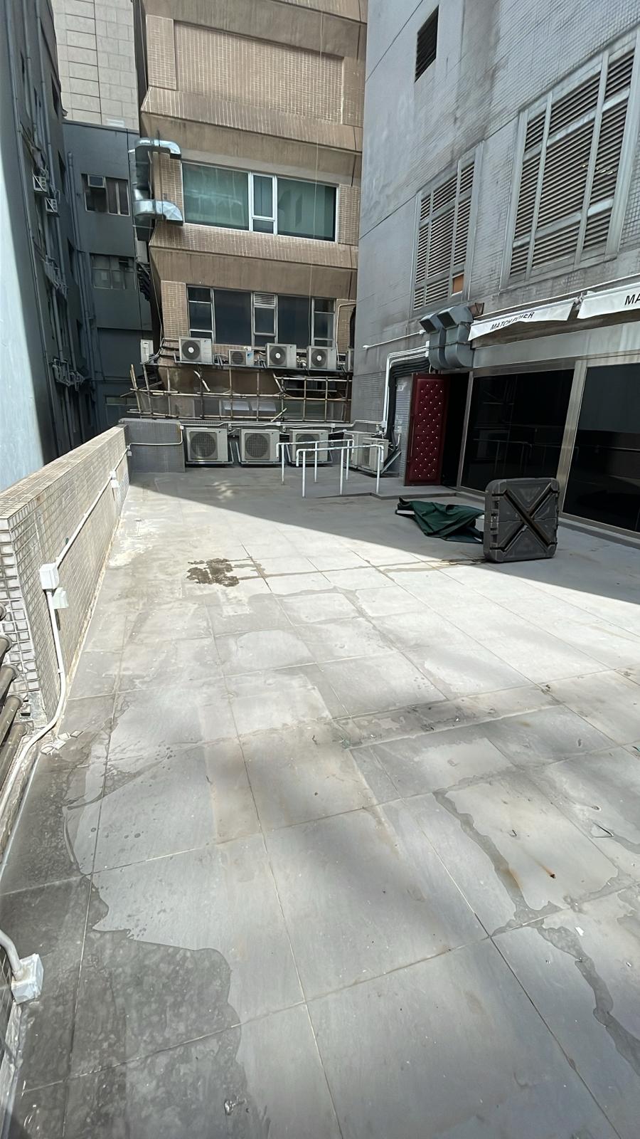 Ref#3602: Sunlit urban rooftop terrace with tiled flooring, scattered furniture, and multiple AC units1perfect for office or restaurant rental opportunities among tall buildings.