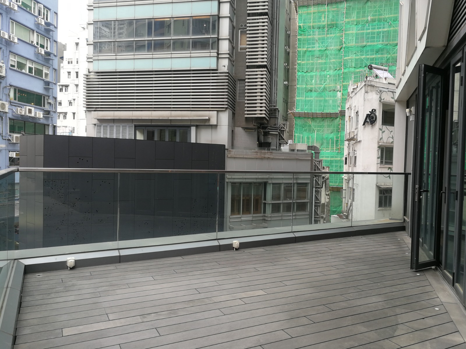 Ref#3597 offers a modern balcony with glass railings overlooking tall buildings, a green net-covered construction site, and high-rises013perfect for renting office or shop space in a lively urban cityscape.