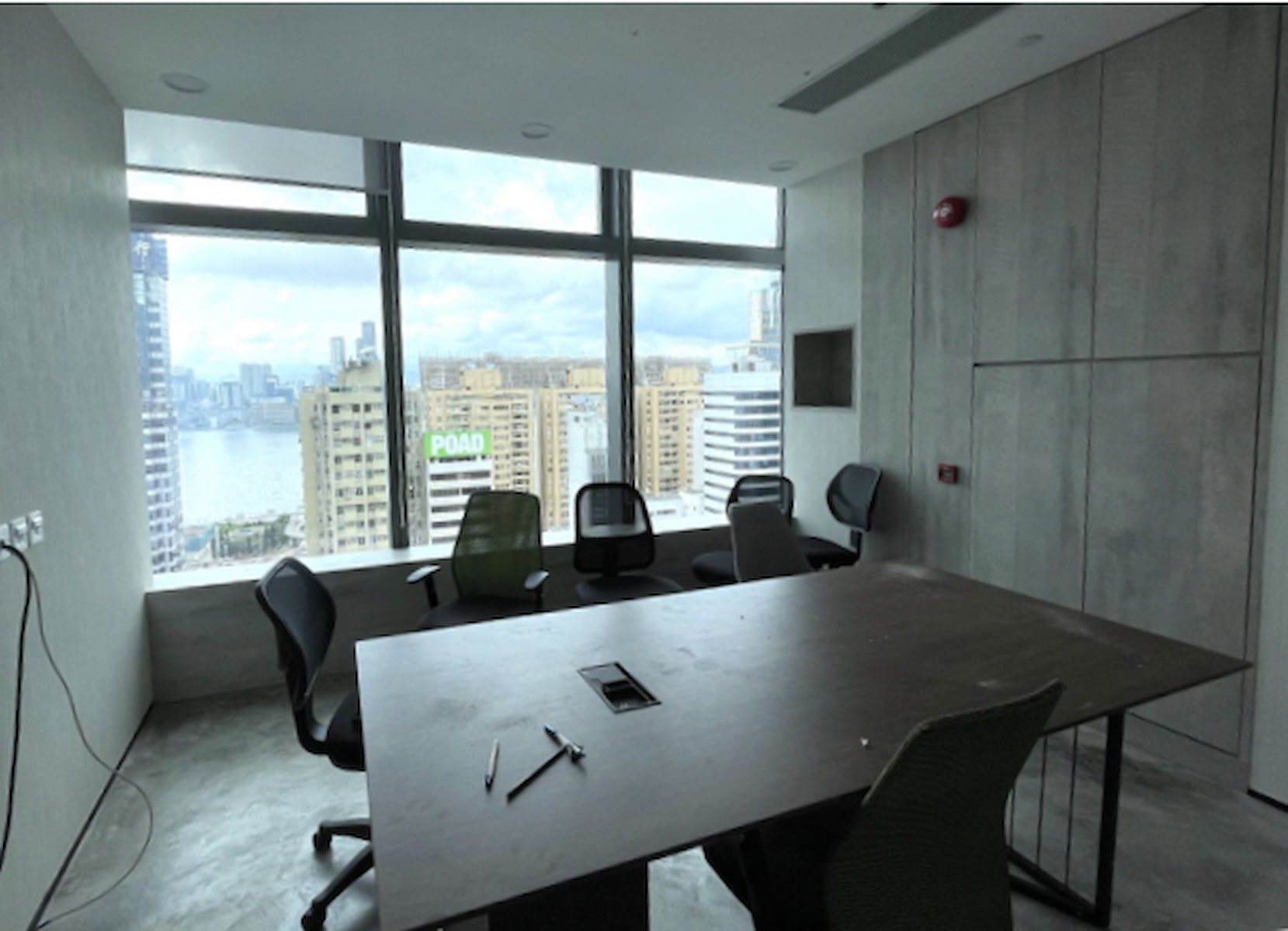 Ref#3281: Modern office for rent with a large desk, five chairs, gray minimalist decor, and expansive windows offering stunning views of skyscrapers and water. Pens and papers are provided on the desk.