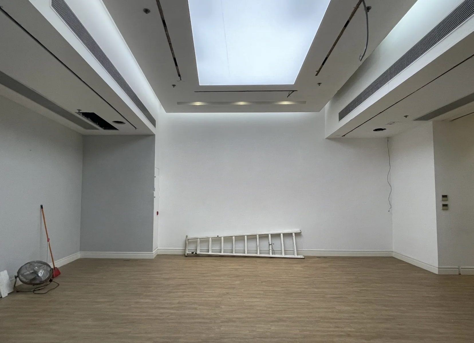 Ref#3355: Minimalist room with light wood floors, white walls, skylight, and ladder. Perfect for use as an office or shop. Comes with a broom and floor fan in the corner for added convenience.