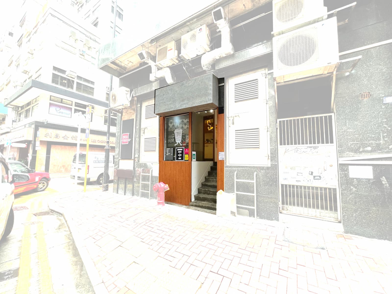 Exterior street view of Ref#3129: building entrance with stairs and a blank sign above the door, ideal for restaurant rental or lease. Features air conditioning units, sidewalk fire hydrant, and an overexposed photograph.