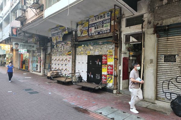 A man in a mask walks past closed storefronts and rent ads on a quiet, worn city street beside two parked carts as another person passes in the background. Product shown: Ref#3578.