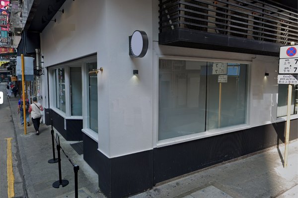Ref#3258: Corner building with large windows and a blank round sign above the entranceideal to rent office or shop space. A person walks by on the sidewalk; a no parking sign is visible on the street.