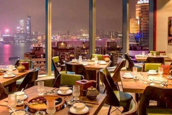 Ref#3441 is a modern restaurant for rent with large windows showcasing panoramic city skyline and waterfront views at night, where city lights reflect on the water and neatly set tables enhance the elegant atmosphere.