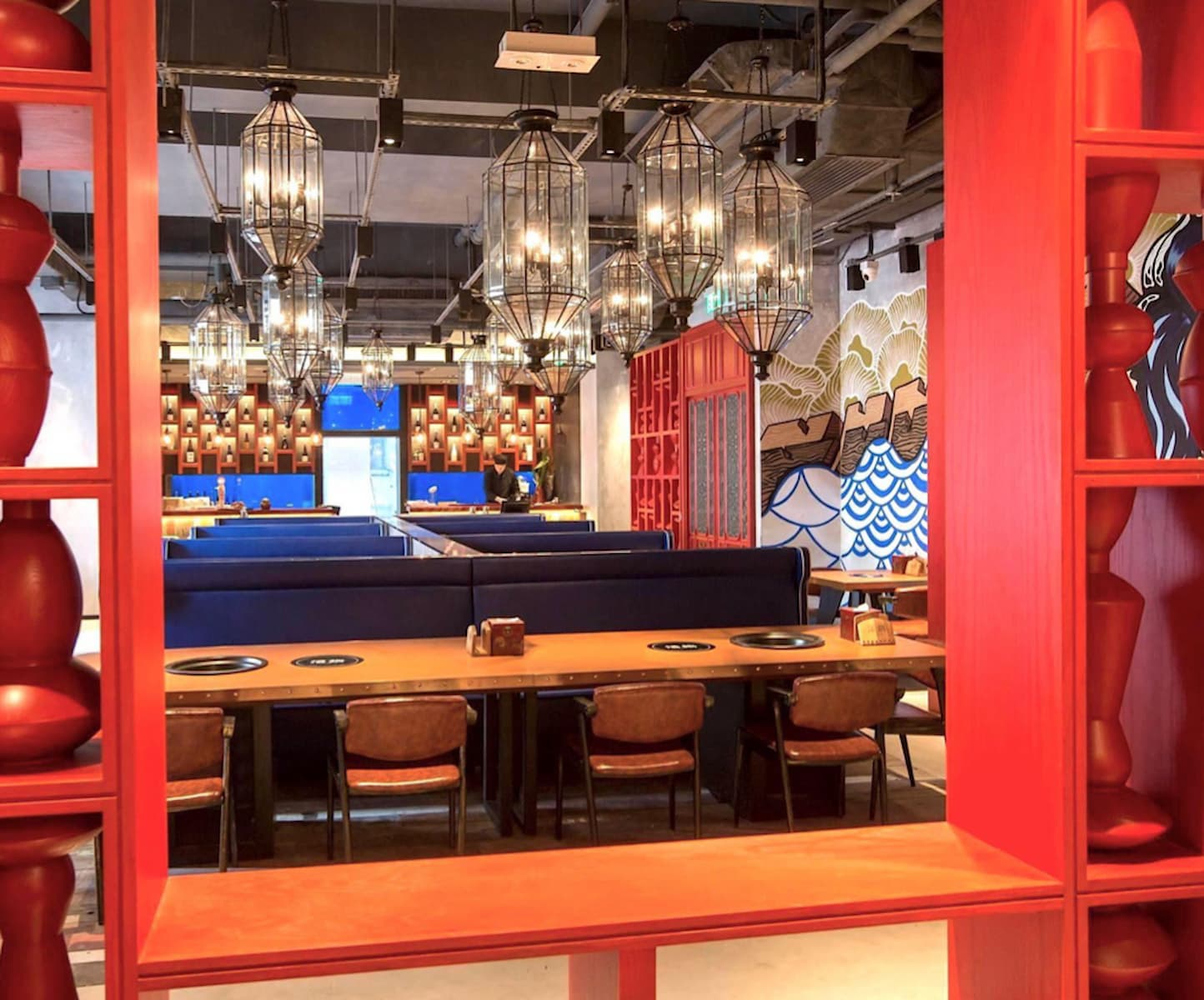 Ref#3441 features a modern restaurant interior with blue booths, wooden tables, and brown chairs. Lantern lights hang above, red shelves frame the view, and a bold-patterned mural decorates the back wall9perfect for restaurant rentals.