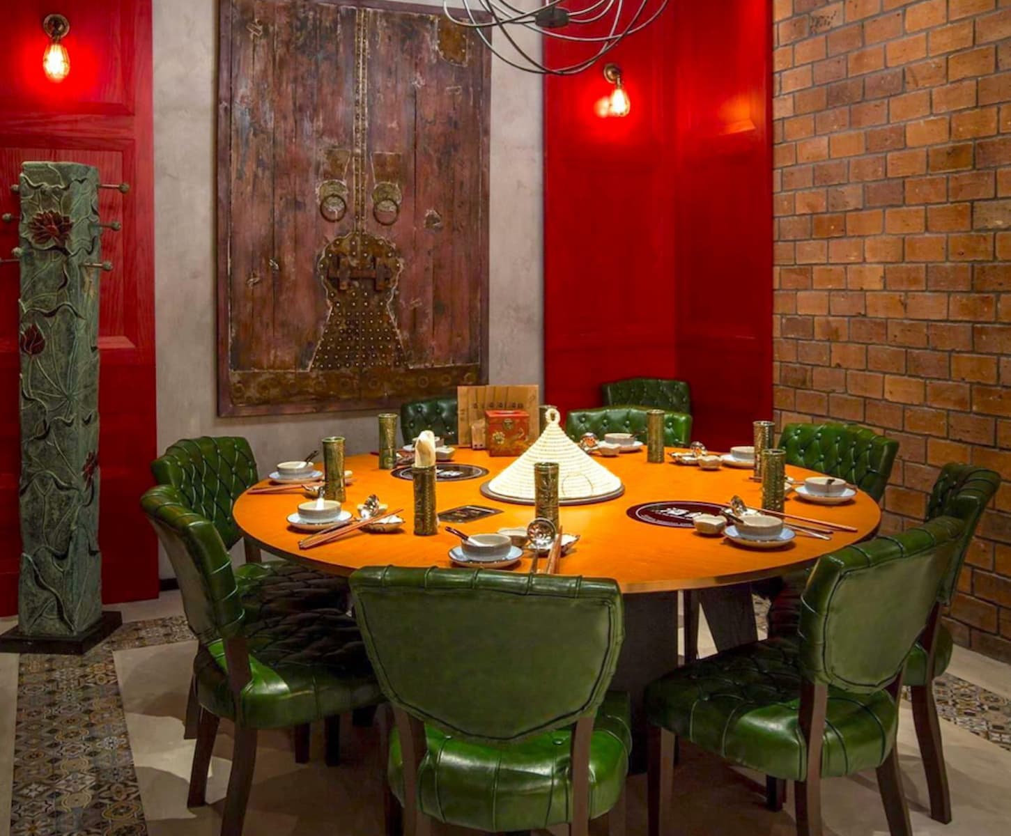 Ref#3441: A round dining table for eight with green cushioned chairs, decorative plates, chopsticks, and gold glasses stands in a vibrant room with red walls, brick accents, and ornate artwork9ideal for restaurant rentals.