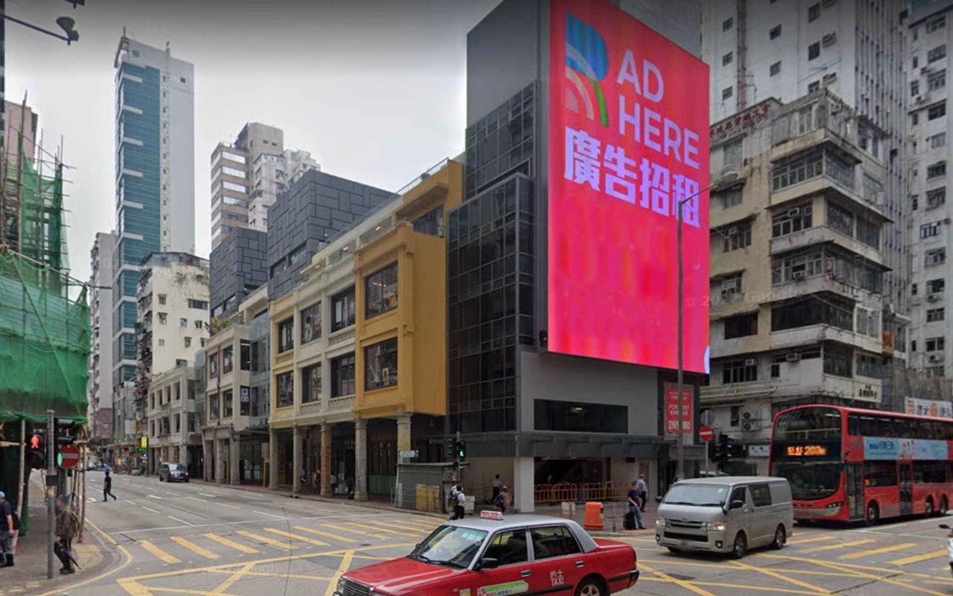 Ref#3505: A busy city intersection with old and modern buildings, a blank digital billboard reading AD HERErent office,	2 a red taxi in front, and a double-decker bus on the right.