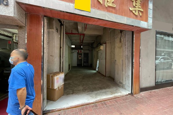 A man wearing a blue shirt and face mask walks by Ref#3257, an open, empty storefront with exposed walls and ceiling pipes. Two cardboard boxes rest near the entrance on the tiled sidewalk00an ideal rental for shop or restaurant use.