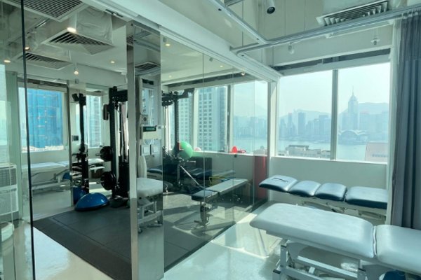 Ref#3421: A bright, modern space ideal for office rental or physical therapy with large windows, exercise equipment, treatment tables, and a city view. Sunlight fills the area through glass walls and windows.