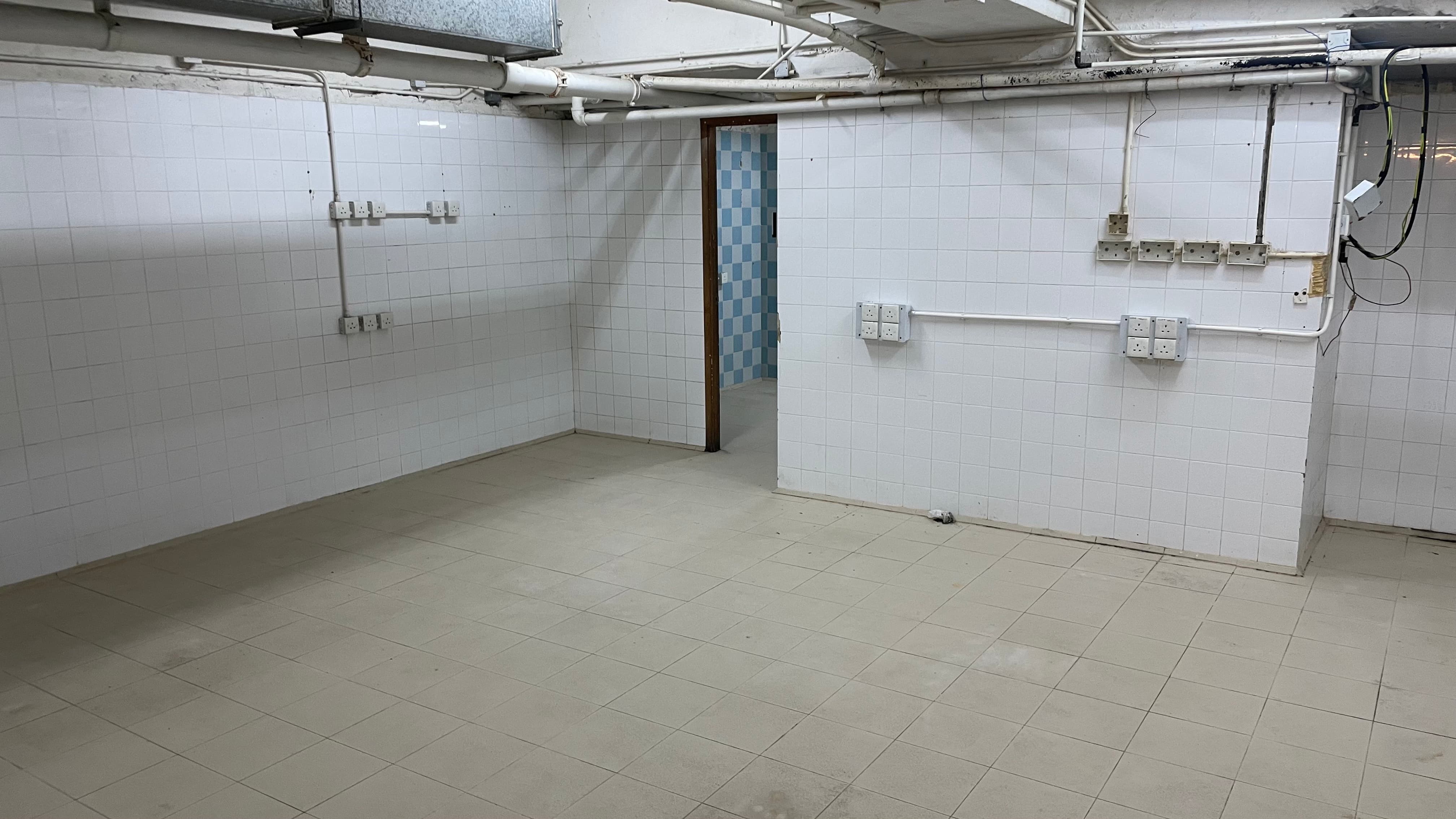 Ref#3494: Empty room with tiled floors, white tiled walls, exposed pipes, and outlets
d�perfect for a shop or office. Features an open doorway to another room with blue and white checkered tiles.