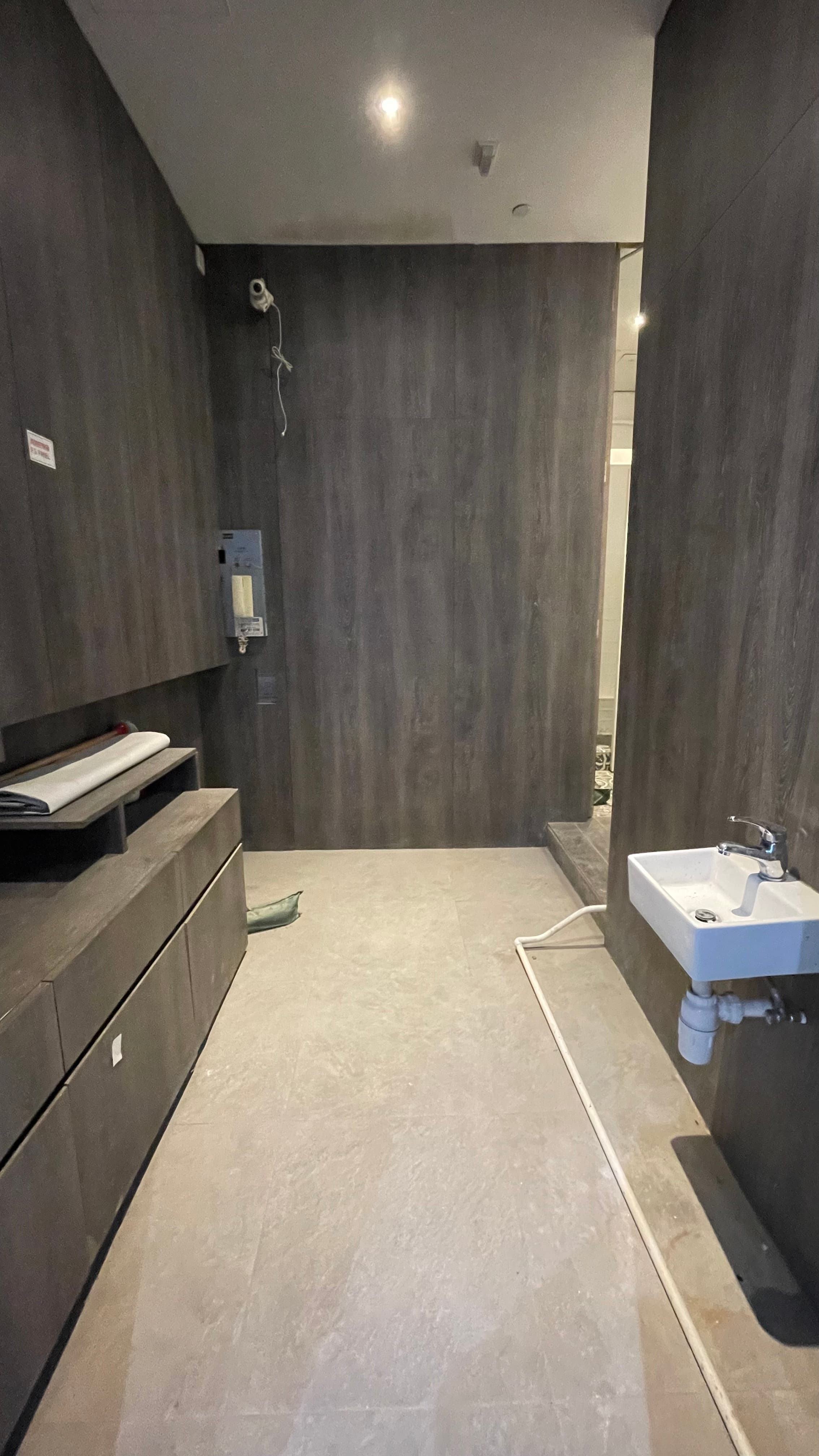Ref#3494: Mostly empty room with dark wood-paneled walls, small white sink, water heater, and light grey tiled floor
d�perfect for shop or office rental. Exposed pipes and cables allow easy access.