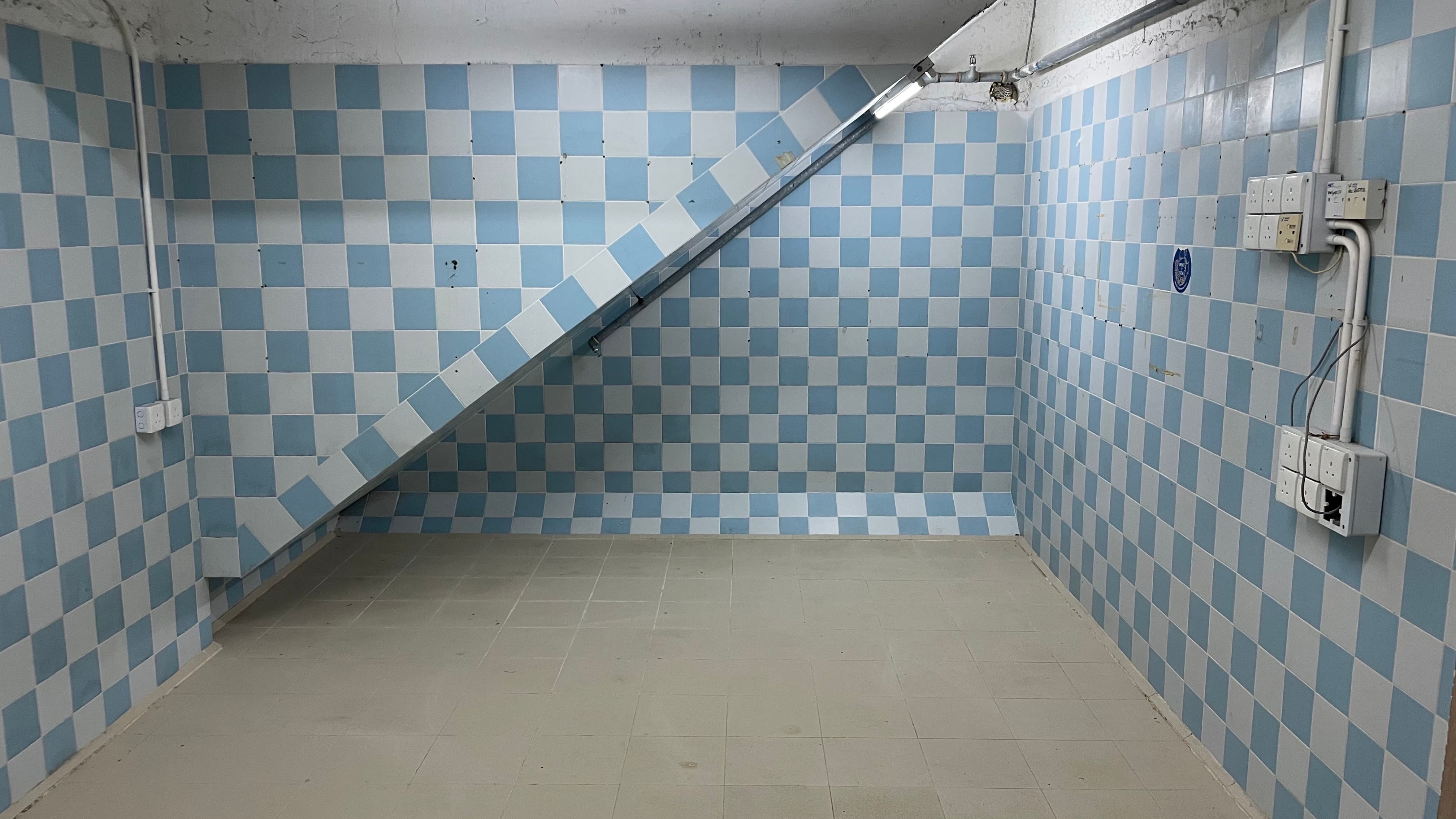 Ref#3494: Small, empty room with light blue and white checkerboard tiled walls, beige floor tiles, and staircase with matching tiles
d�ideal for office or shop use. Electrical panels mounted on right wall.