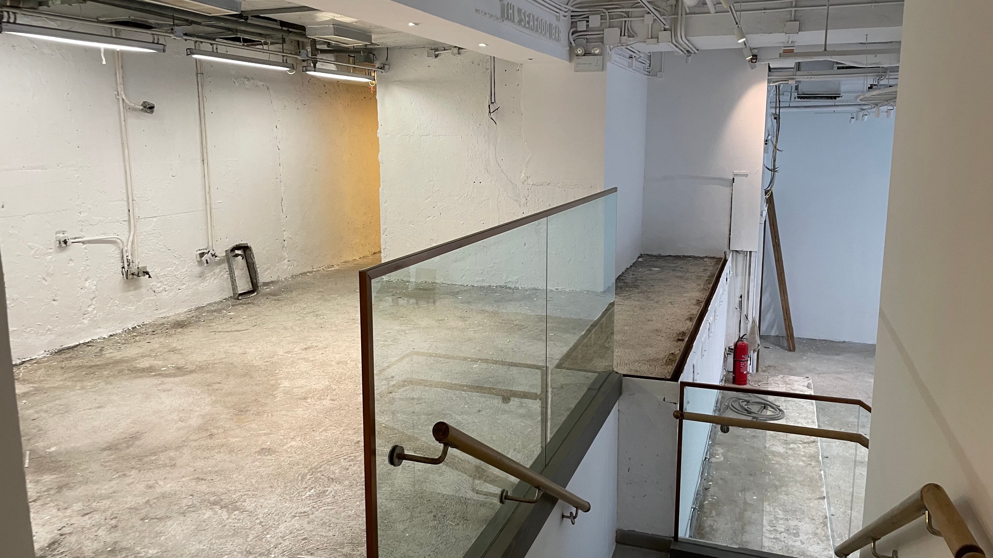 Ref#3494 features an unfinished interior with bare concrete floors, white walls, exposed pipes and ceiling
d�ideal for office or restaurant rental. Glass railing and stairs lead to another level where a red fire extinguisher is visible.