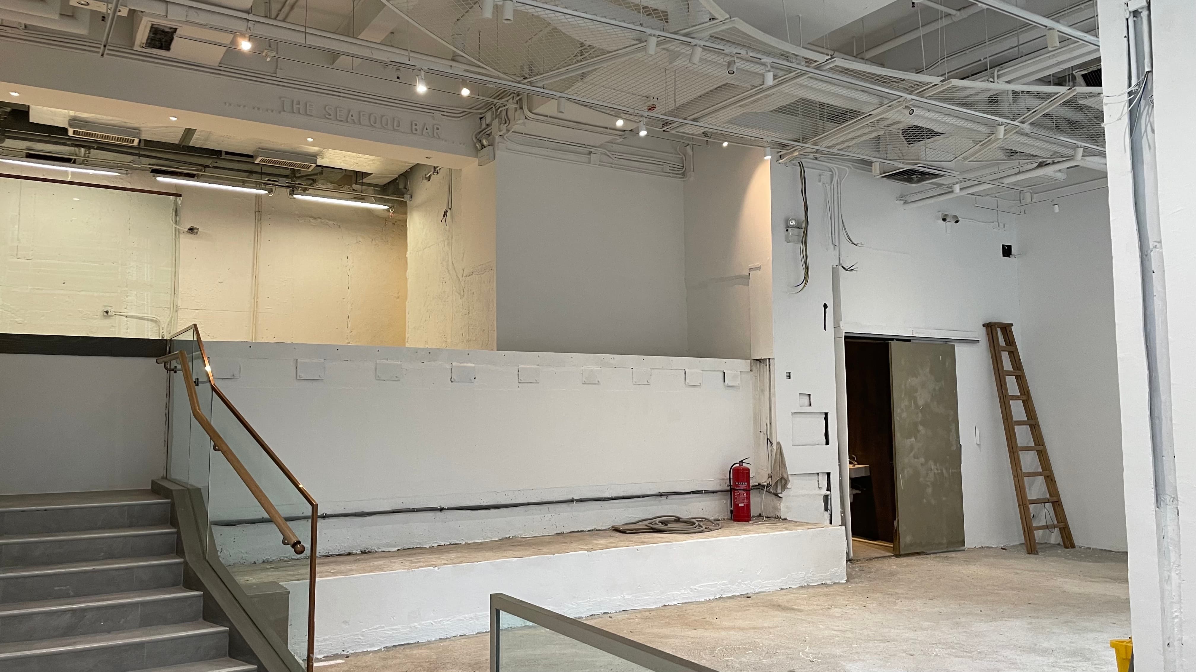 Ref#3494: Empty, unfinished commercial space for rent
d�great for a shop, office, or restaurant. Features white walls, exposed ceiling pipes, staircase with railing, raised platform, fire extinguisher by the door, and scattered construction materials.