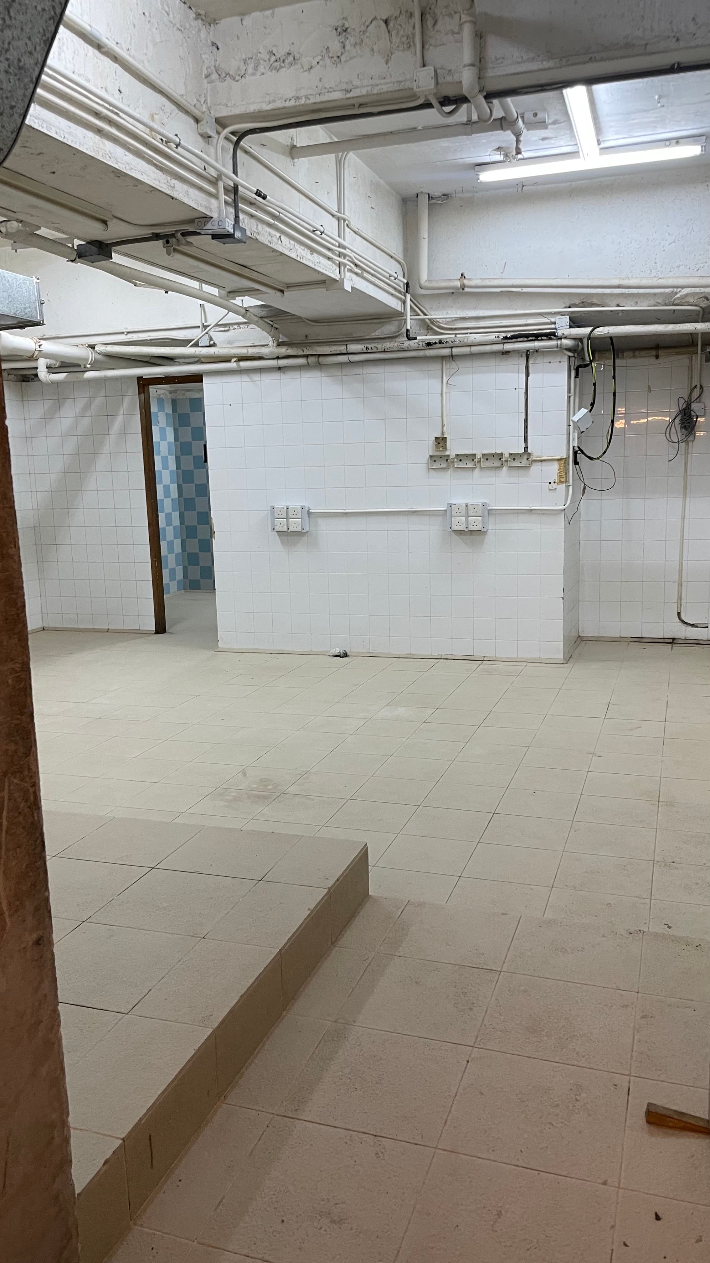 Ref#3494 features a spacious, tiled basement with exposed ceiling pipes, white tile walls, visible wiring, and an open doorway to another tiled space
d�perfect for renting as an office or shop.